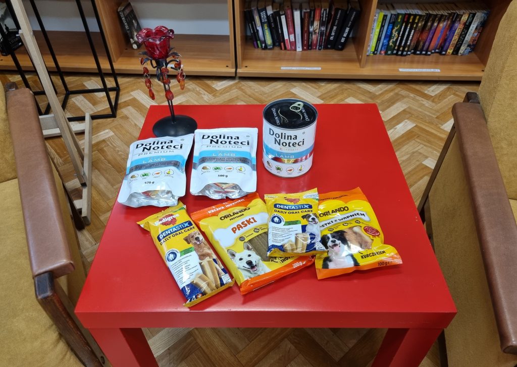 Na czerwonym stoliku saszetki, puszka i naturalne gryzaki dla psa