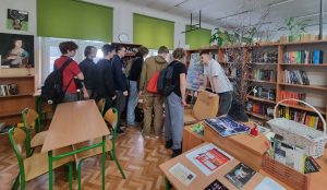 Grupa młodzieży w bibliotece szkolnej przyglądająca się wystawie
