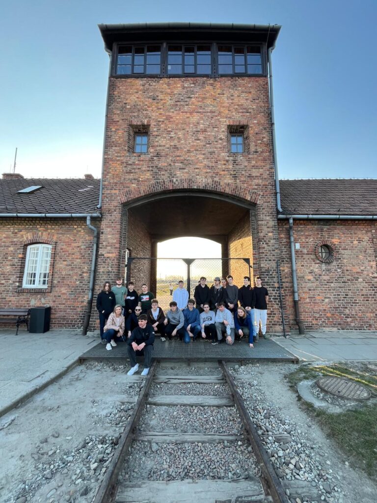 Zdjęcie grupowe na tle bramy nazistowskiego obozu koncentracyjnego w Auschwitz-Birkenau